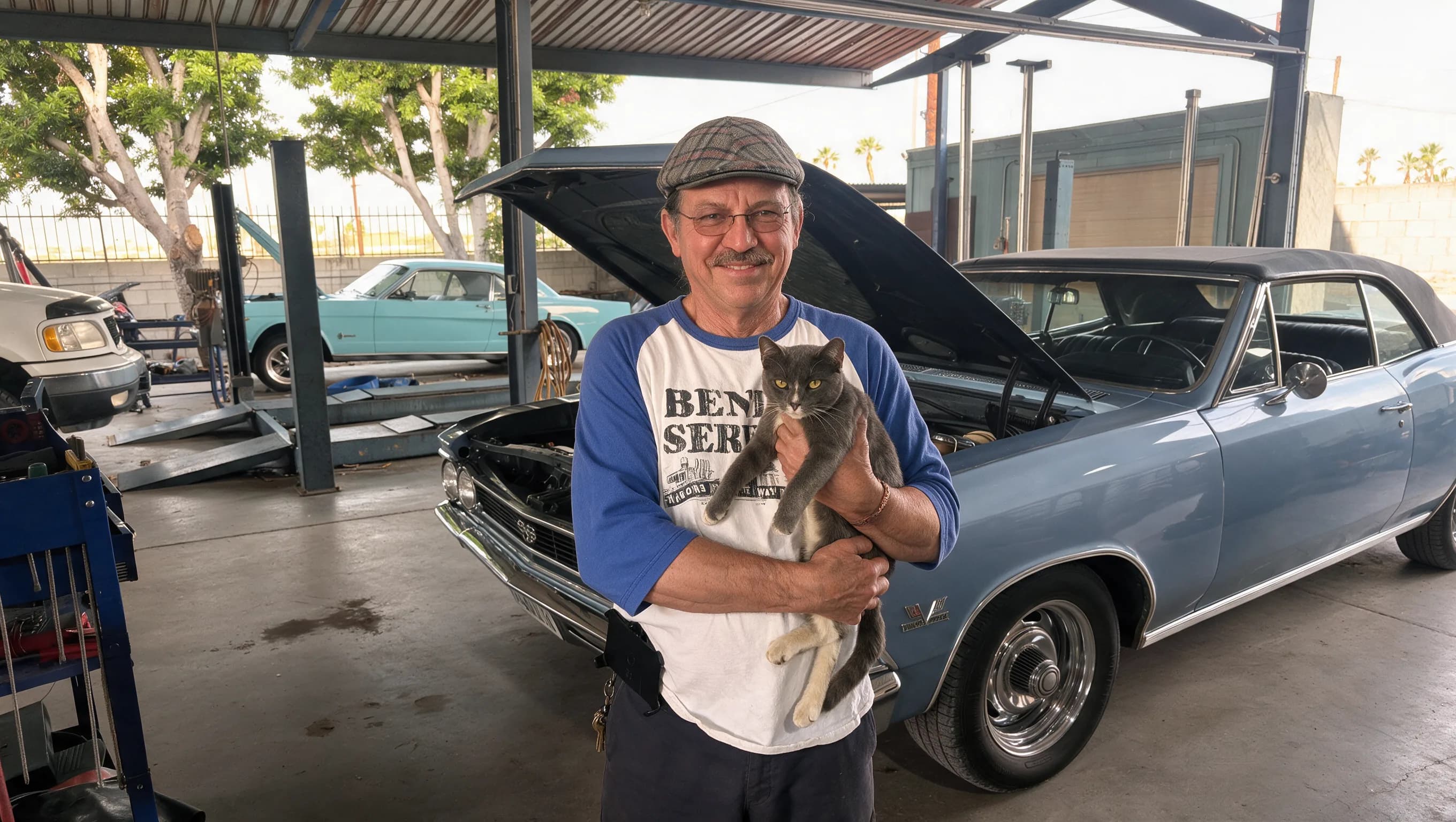 Pete holding the shop cat in front of a classic Chevelle at Pete's Automotive Service